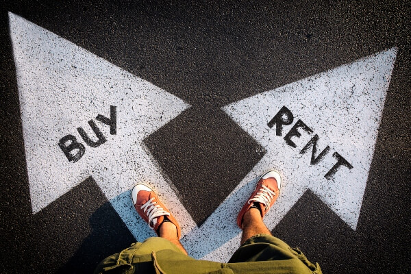 A person stands with each foot on a different arrow. One arrow says rent, the other says buy.