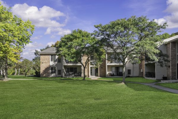 Apartment building with green lawn and trees under a clear blue sky.