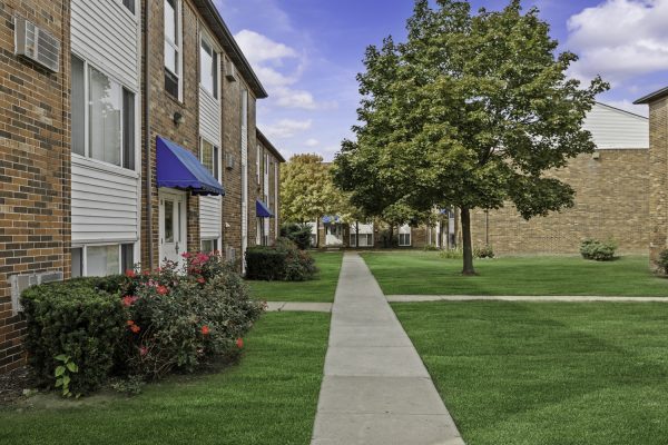 Brick apartment buildings with blue awnings, green lawns, and trees on a sunny day.