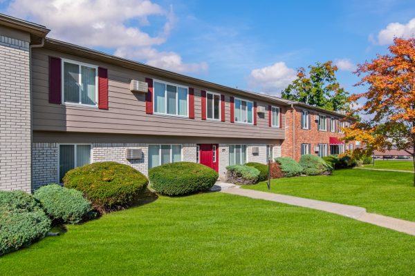 Two-story apartment building with green lawn, red doors, and autumn trees under a blue sky.