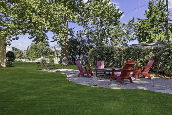 Outdoor patio with pink Adirondack chairs on a lush green lawn for relaxing in a garden setting under clear blue skies.