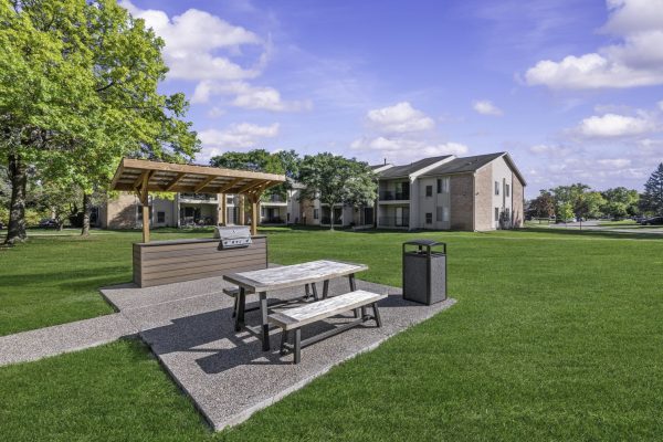 Outdoor picnic area with a grill and seating in a lush green neighborhood, surrounded by residential buildings.