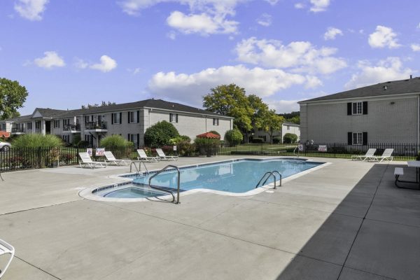 Outdoor pool with lounge chairs and residential buildings under a clear blue sky.