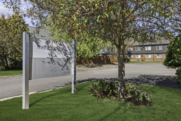 Metropolitan Flats sign with building in background, tree and greenery in foreground, sunny day.