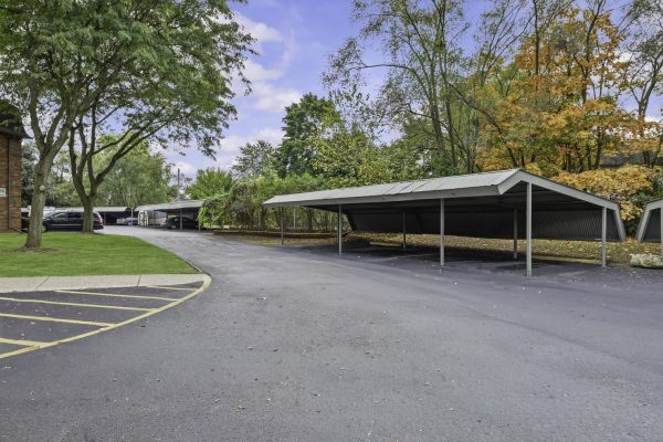 Covered parking area with cars and colorful autumn trees, under a blue sky.