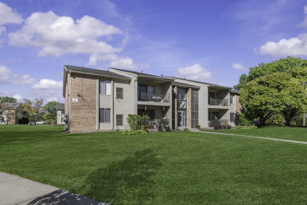 Modern apartment building with brick facade, green lawn, and blue sky background.