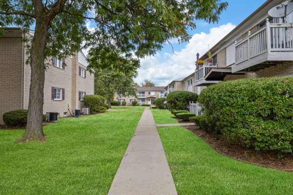 Pathway between brick apartment buildings with green lawns and trees under a clear blue sky.