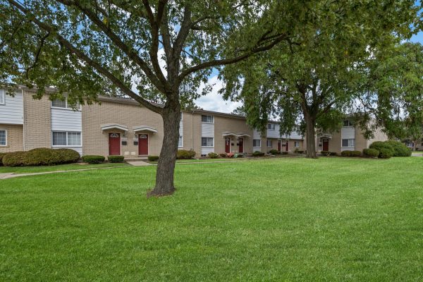 Row of townhouses with red doors and lush green lawn under a clear blue sky.
