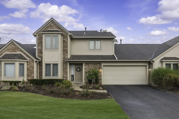 Modern suburban home with brick and siding exterior, two-car garage, and well-manicured lawn under a blue sky.