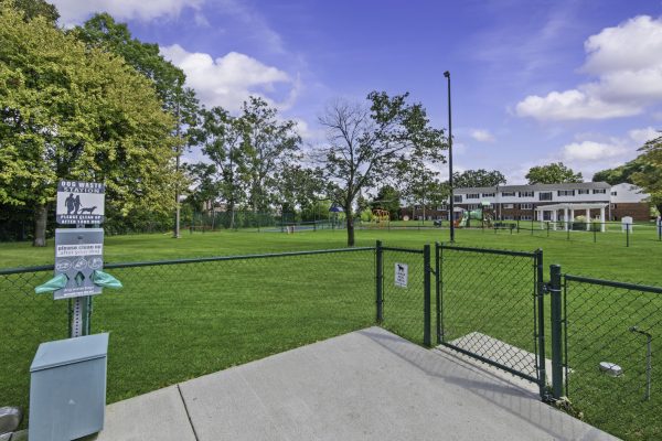 Dog park with waste station, fence, and playground in a residential neighborhood on a sunny day.