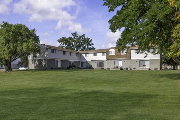 Wide lawn in front of a row of suburban townhouses with a blue sky backdrop.