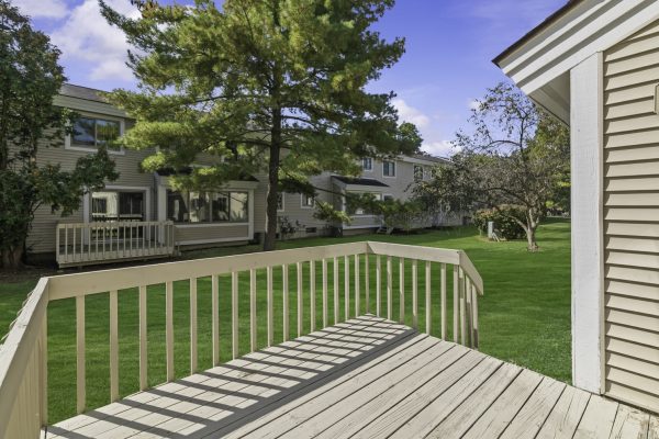 Spacious backyard view from wooden deck, surrounded by trees and greenery, ideal for relaxation.