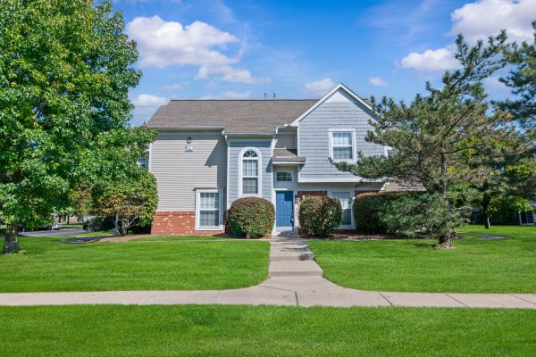 Suburban house with manicured lawn, green trees, and clear blue sky on a sunny day.