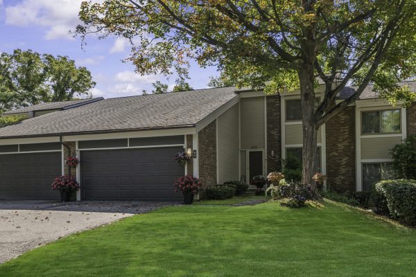 Modern suburban house with garage, surrounded by lush green lawn and trees under a clear blue sky.