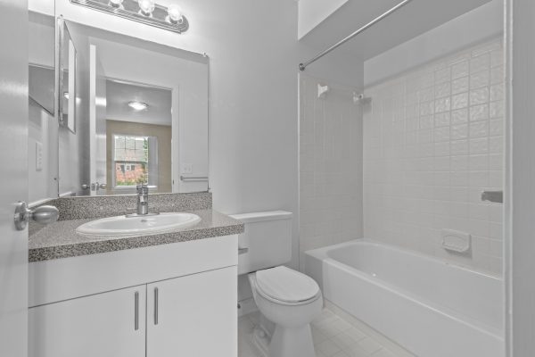 Modern white bathroom with granite countertop, mirror, toilet, and bathtub with tiled walls.