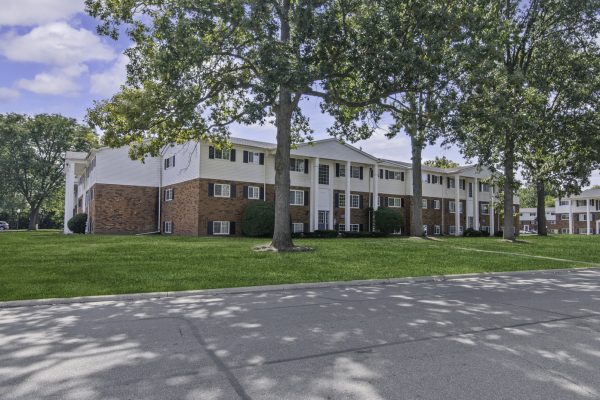 Apartment building with brick facade surrounded by trees and green lawn under a blue sky.