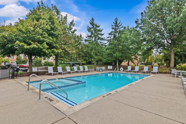 Outdoor swimming pool with lounge chairs and surrounding trees on a sunny day.