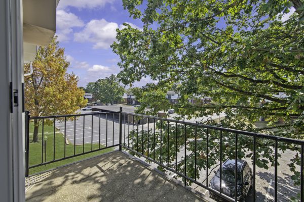 View from a balcony overlooking a parking lot, trees, and suburban neighborhood under a blue sky.
