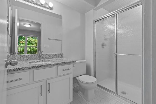 Modern bathroom with granite countertop, shower, and window view. Bright lighting reflects off clean, white fixtures.