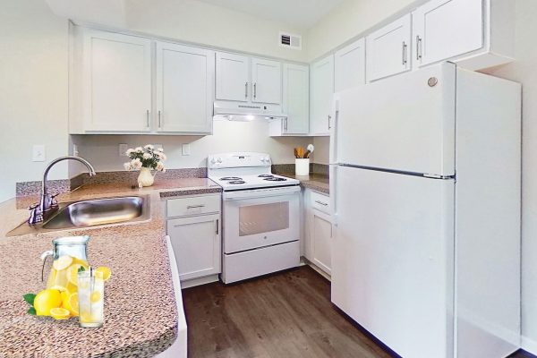 Modern white kitchen with granite countertops, vase of flowers, and a lemon drink pitcher on the counter.