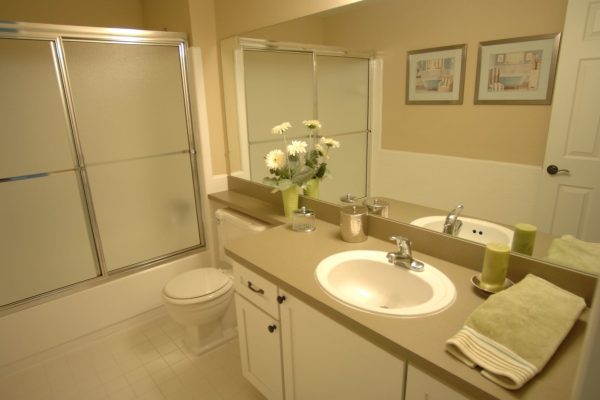 Modern bathroom with beige countertop, mirror, daisy vase, green candles, and glass shower door.