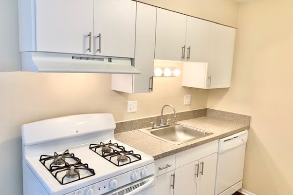 Modern kitchen with white cabinets, gas stove, stainless sink, and dishwasher for efficient culinary convenience.