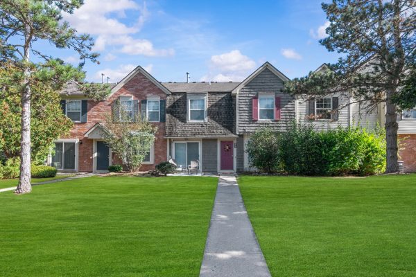 Two-story suburban townhouse with green lawn and a pathway under a blue sky.