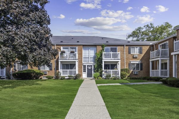 Red brick apartment building with green lawn, balconies, and blue sky background.