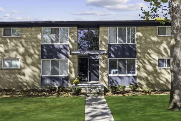Mid-century modern apartment building with brick facade and blue accents, surrounded by a green lawn.