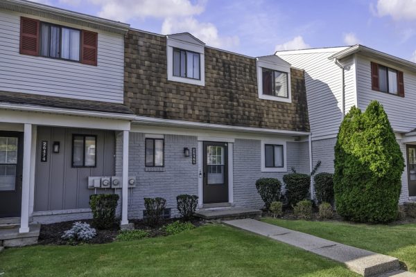 Townhouse exterior with modern design, brown shingles, white siding, and green lawn under a clear sky.