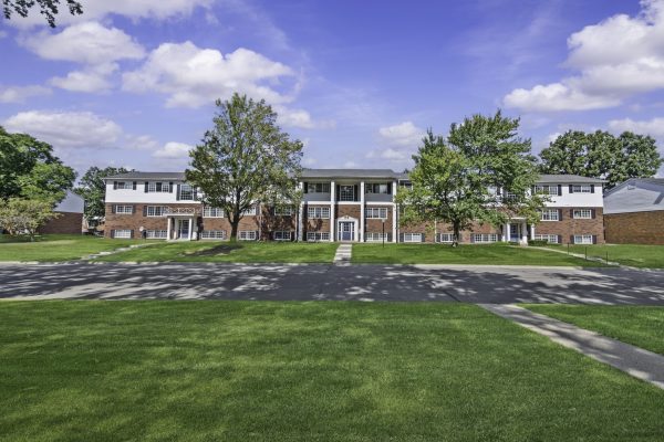 Brick apartment building with green lawn, trees, and clear blue sky background.