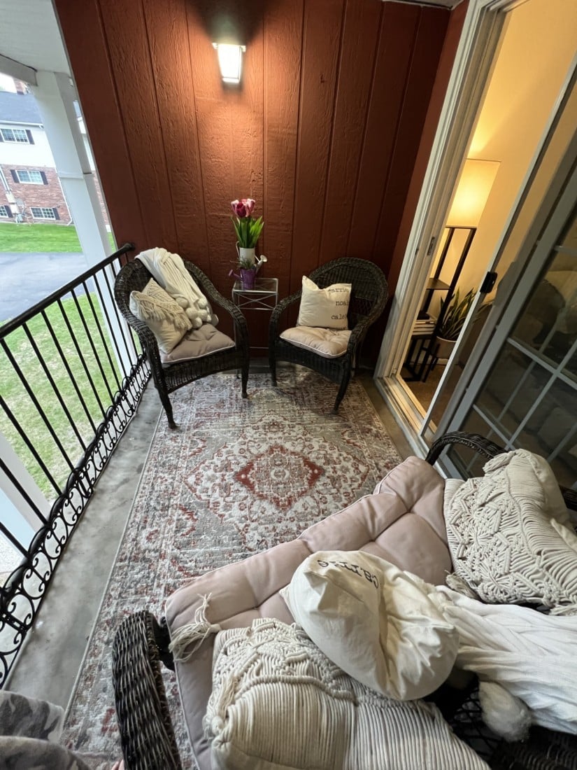Cozy balcony seating with woven chairs, pillows, and a rug, perfect for relaxation.