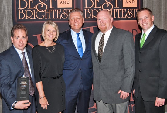 Group photo of business professionals at an award event, posing in front of Best and Brightest banner.