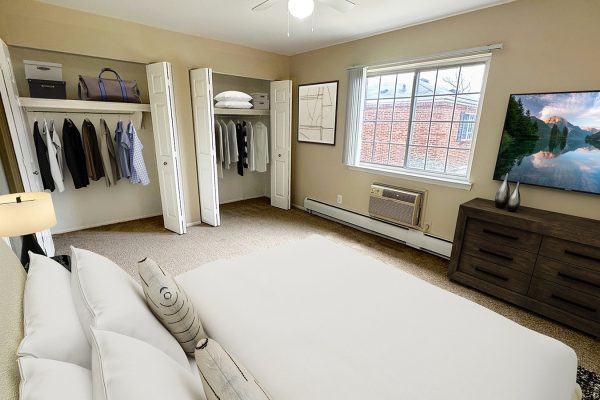 Modern bedroom with open closets, cozy bed, dresser, and large window with scenic view on TV.