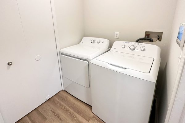 White washing machine and dryer in a compact laundry room with wood flooring.