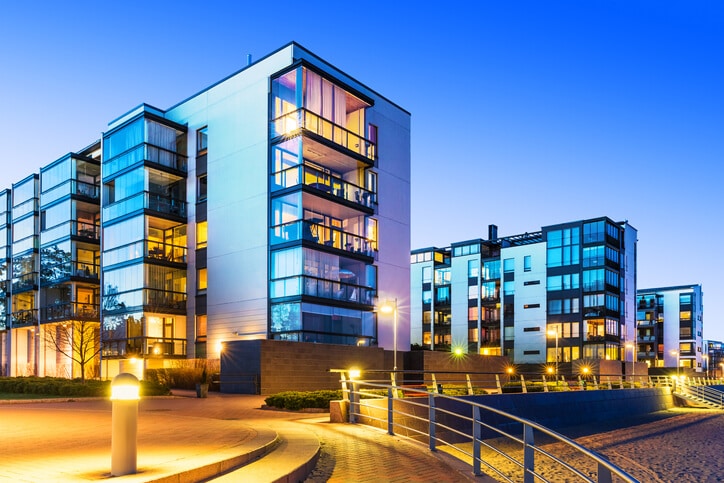 Modern apartment buildings at sunset with illuminated windows, featuring a pathway and railing in the foreground.