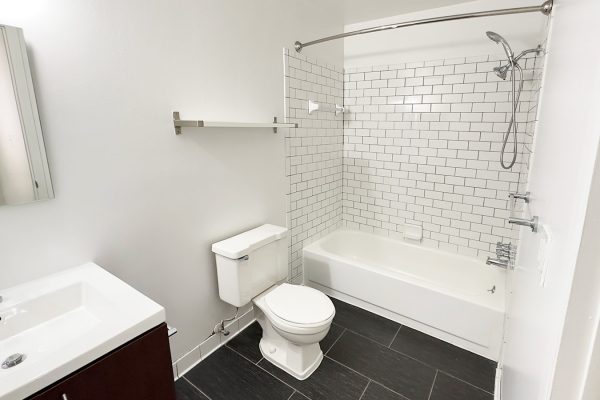 Modern bathroom with white subway tiles, shower, sink, and toilet on dark tiled floor.