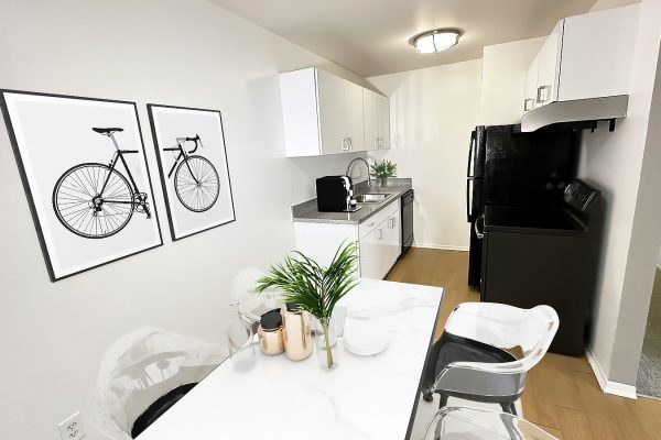 Modern kitchen with white cabinets, black appliances, and bicycle wall art. Cozy dining table with plants.