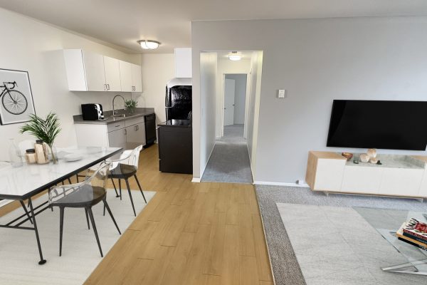 Modern open-plan living area with a kitchen, dining table, minimalist decor, and wall-mounted TV.