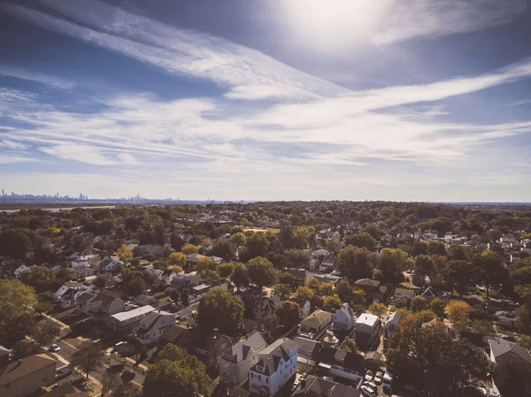 Aerial view of a suburban neighborhood under a clear, sunny sky with distant city skyline in the background.