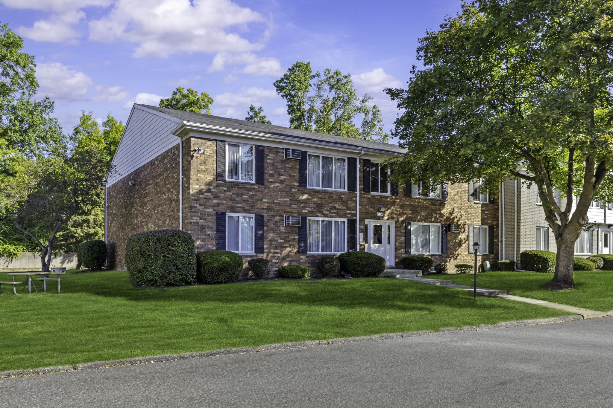 Brick apartment building with lush greenery and blue sky background.