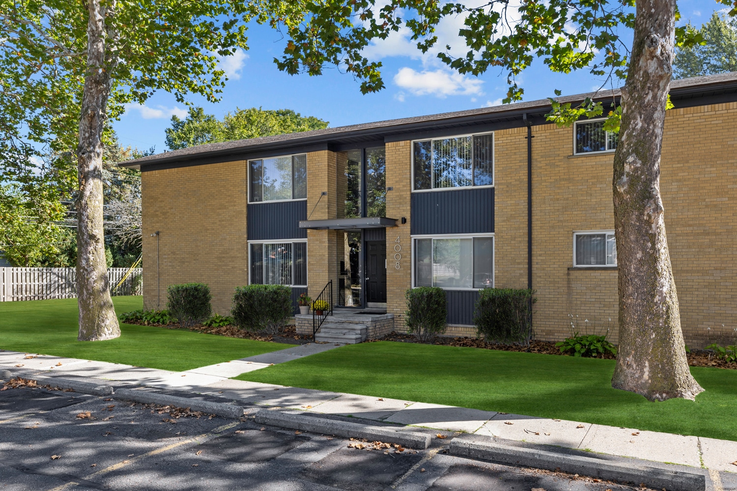 Exterior of a two-story brick apartment building with manicured lawn and surrounding trees.