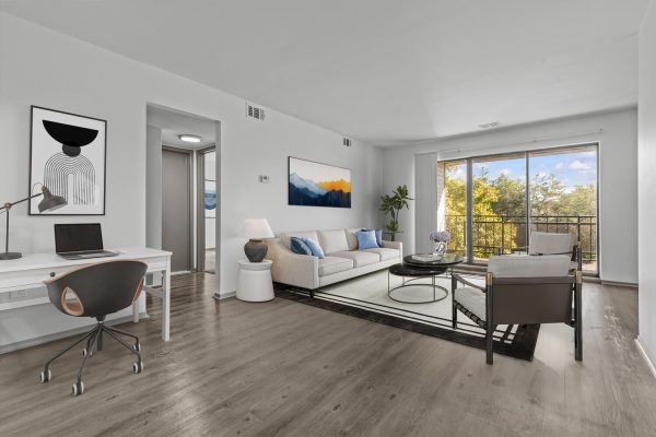 Modern living room with balcony, sofa, artwork, and home office desk. Bright and spacious interior design.