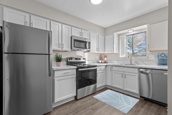 Modern kitchen with white cabinets, stainless steel appliances, and a window view.