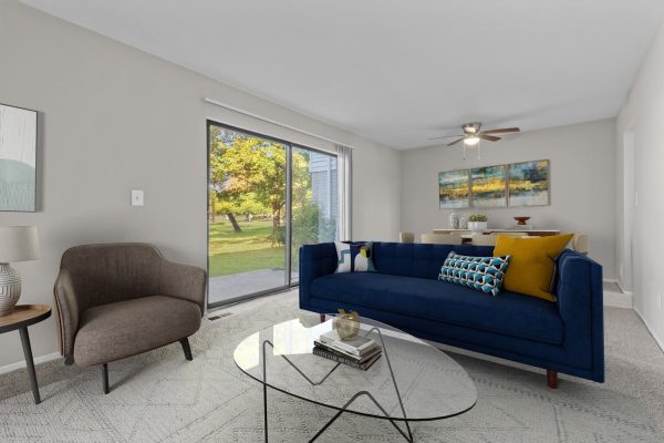 Modern living room with blue sofa, armchair, glass coffee table, and large window view of garden.