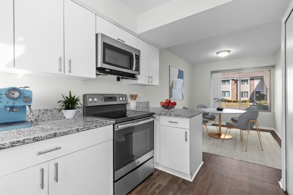 Modern kitchen with white cabinets, stainless steel appliances, and dining area with large window and contemporary chairs.