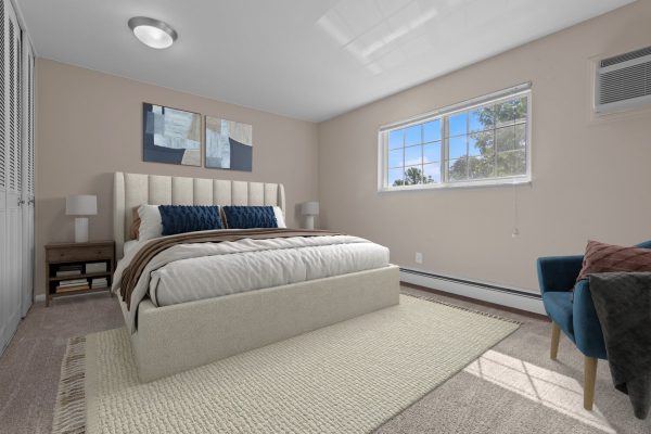 Modern bedroom with beige walls, king-size bed, blue pillows, and large window with natural light.