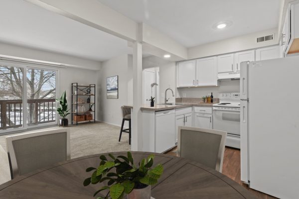 Modern open-concept kitchen and living room with white cabinetry and large window overlooking a balcony with trees.