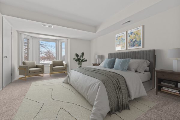 Modern bedroom with gray bedding, stylish chairs, and large window, featuring cozy decor and wall art.